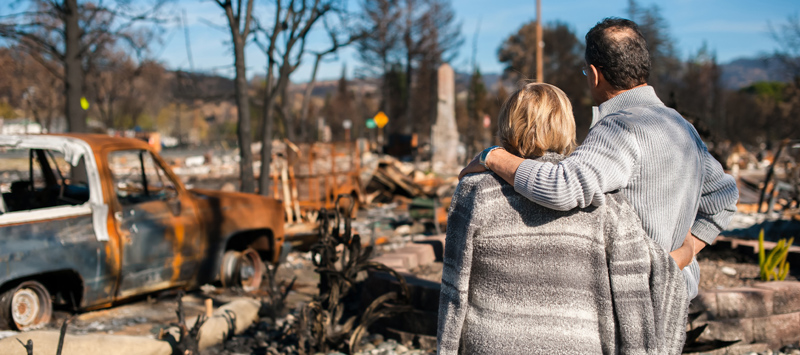 Man and woman holding each other in front of a burned home